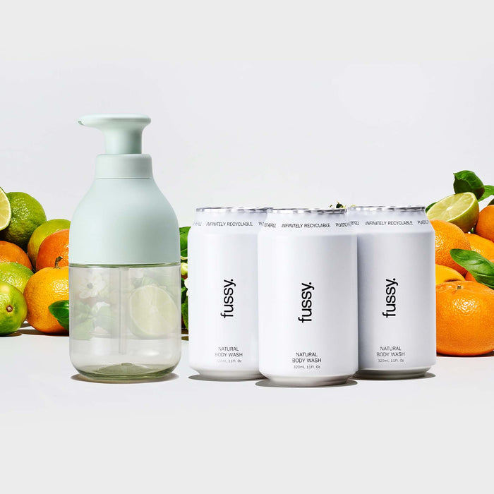 Fussy's Tropic Tonic natural body wash pump bottle with three refill packs, set against a background of limes, mandarins and basil leaves.