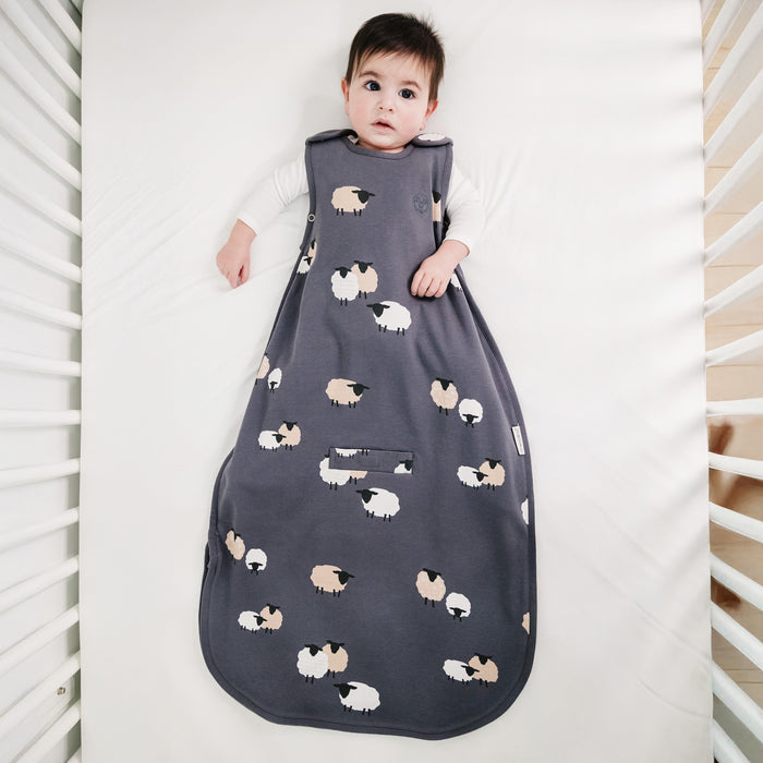 Child wearing a dark gray sleep bag with sheep pattern in a crib.