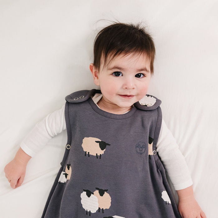 Baby wearing a gray sleep sack with sheep patterns on a white background