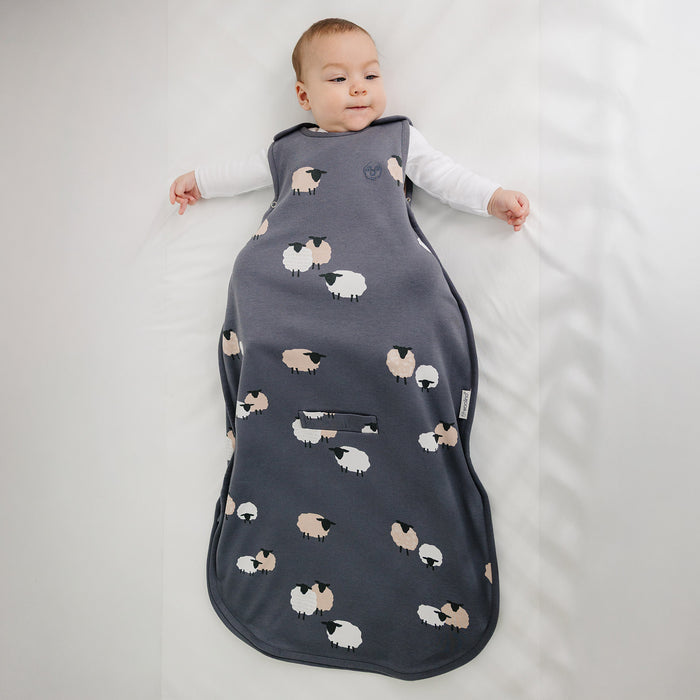 Baby in a dark gray sleep bag with sheep pattern on a light gray background