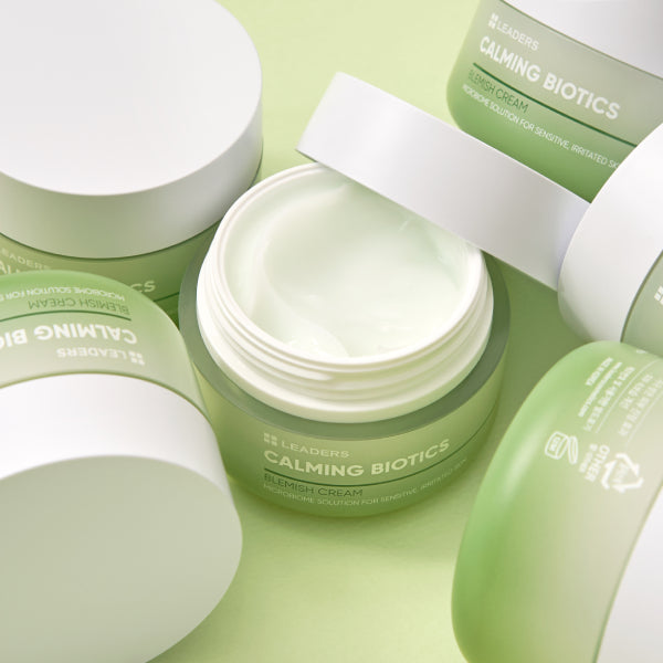 Open jar of Calming Biotics Blemish Cream | Leaders surrounded by closed green and white skincare containers on a light green background.