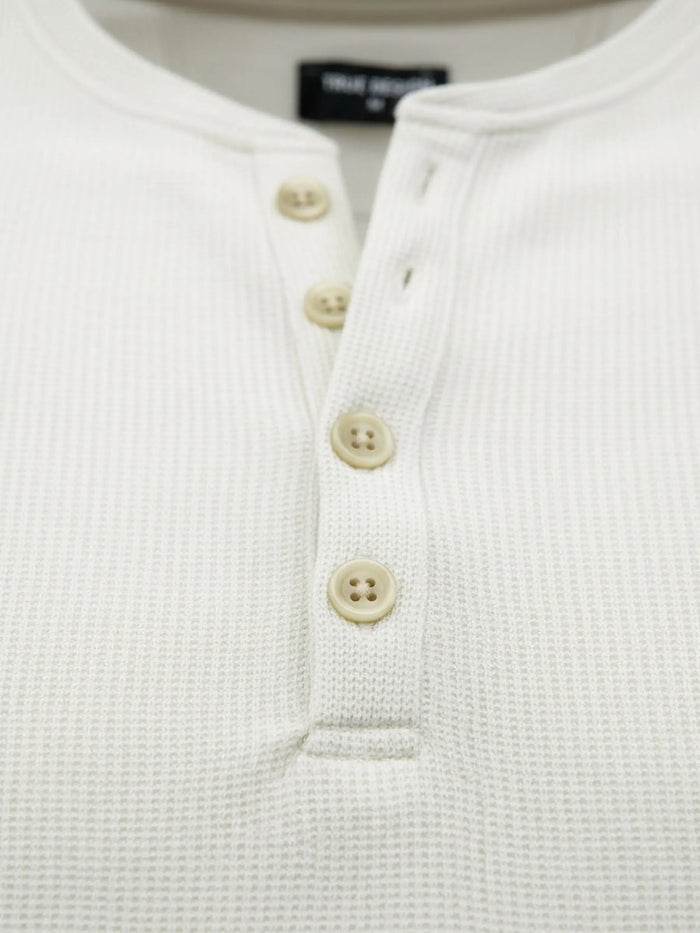 Close-up of off-white sweater buttons and textured waffle knit fabric.
