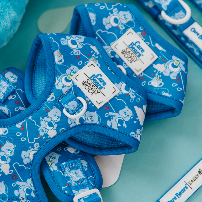 Close-up of Sassy Woof’s Dog Adjustable Harness - Care Bears™ Grumpy Bear, featuring cartoon bears, hearts, and clouds. Blue with white labels and hardware, shown on a light blue background—ideal for Puppy Growth Pawtection Plan pups.