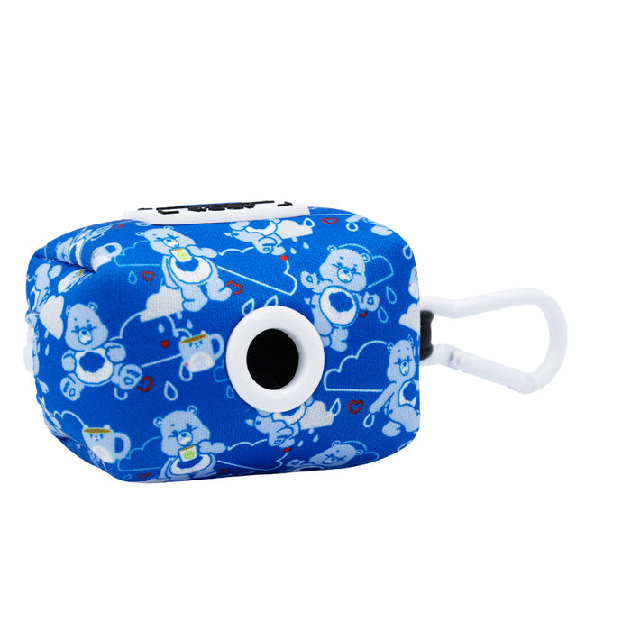 A small, rectangular blue Sassy Woof Dog Waste Bag Holder featuring a white circular port, carabiner clip, and playful Care Bears™ Grumpy Bear design with clouds on a blue background.