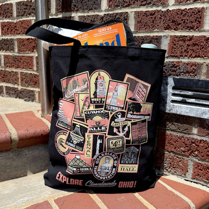 Black tote bag with colorful graphics and text on a brick surface