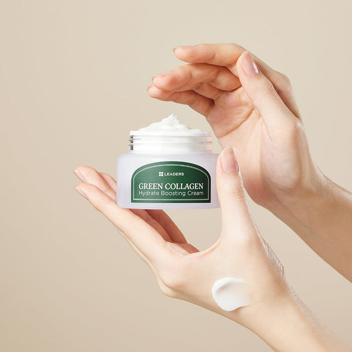 Hands holding an open jar of Green Collagen Firming Hydrate Boosting Cream | Leaders with a small amount of cream on the back of one hand, set against a neutral background.