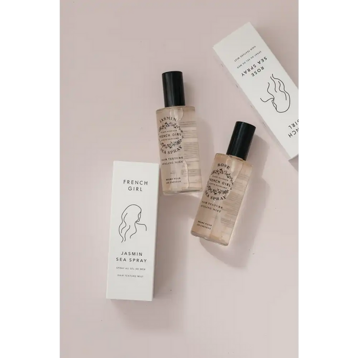 Two clear spray bottles with black caps and minimalist labels alongside white boxes, featuring the product Jasmin Sea Spray - Hair Texture Mist | French Girl on a neutral background.