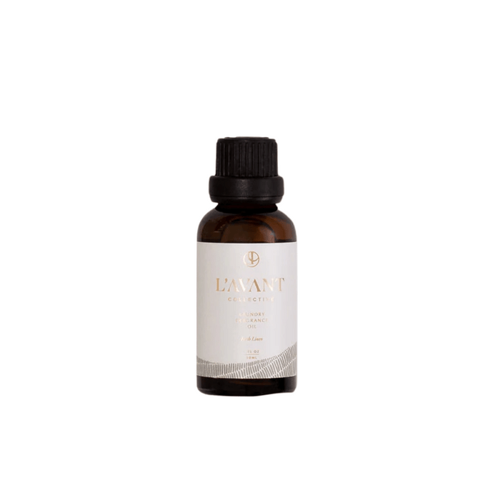 Small amber glass bottle with black cap containing Laundry Oil | L'AVANT Collective, featuring a white label with gold and gray design accents.