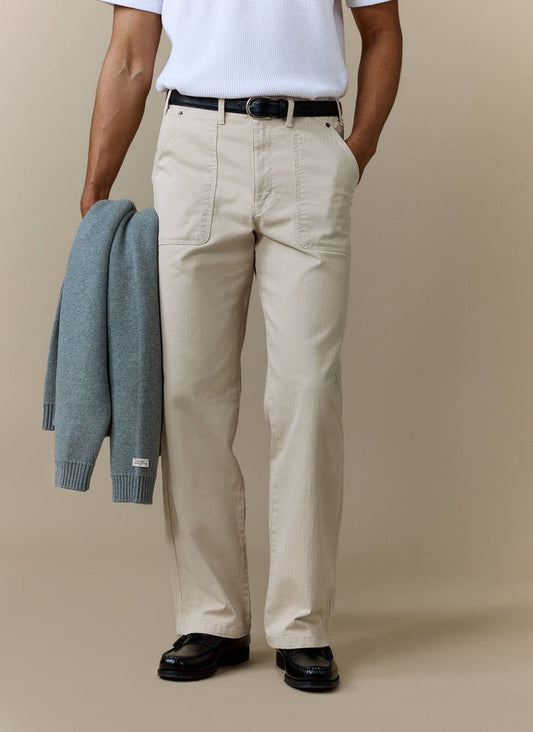A model wears Percival cream carpenter trousers with a white textured t-shirt, black belt, and black loafers.