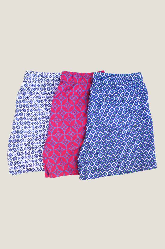 Three pairs of patterned swim shorts in blue and white, pink and blue, and blue and green, displayed side by side on a white background.