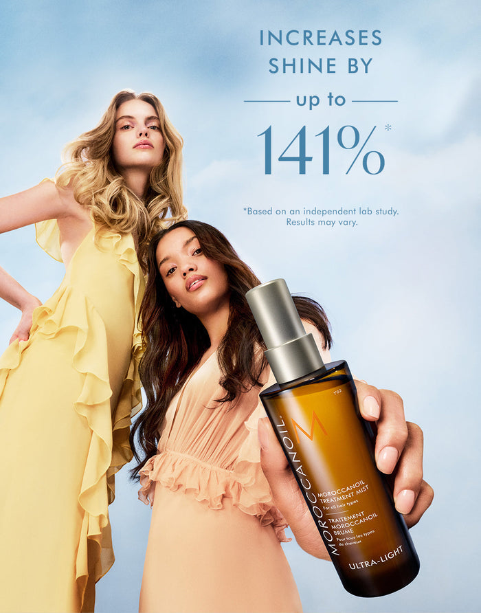 Two women with styled hair pose against a sky background holding a bottle of Moroccanoil Treatment Mist - Full Size | Moroccanoil with text claiming it increases shine by up to 141%