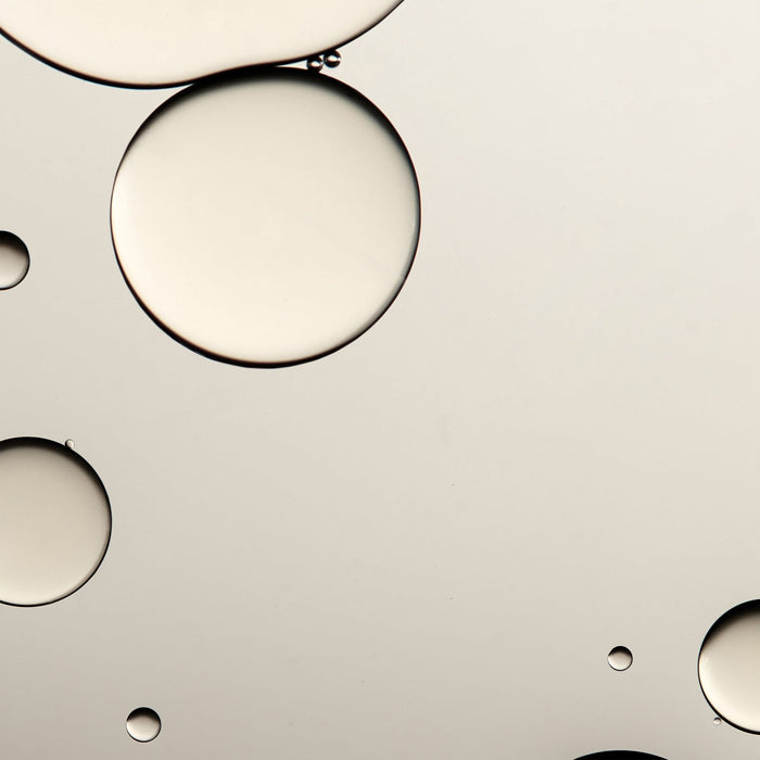Close-up of translucent liquid droplets floating on a smooth surface representing the hydrating and soothing qualities of Queen of Hungary Mist | Omorovicza skincare product.