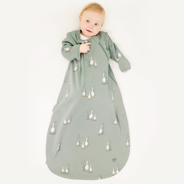 Baby wearing a green sleep bag with sleeves with a duck pattern on a white background