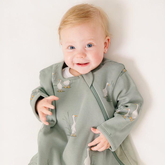 Baby wearing a green sleep bag with sleeves with a duck designs on a white background