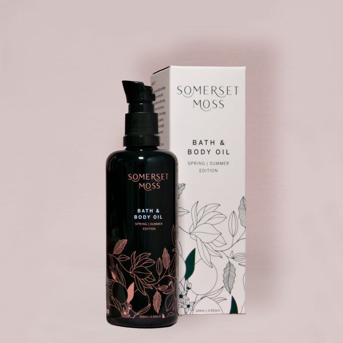 A dark glass bottle with floral design alongside a white box featuring botanical illustrations, both labeled Spring Summer Bath & Body Oil | Somerset Moss for skincare and body care.