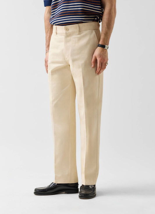 A man models the Percival Straight Leg Chino in ecru, styled with a striped polo shirt and black loafers.