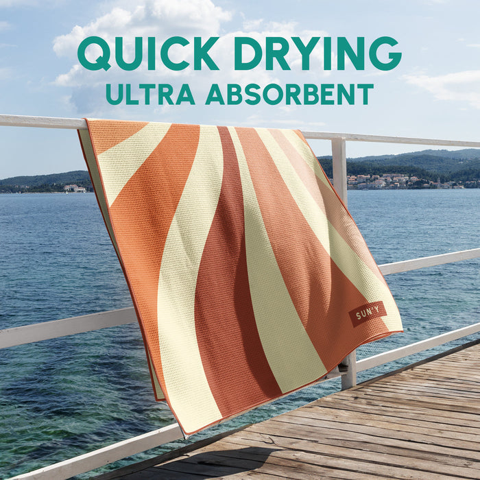 Waffle Microfiber Beach Towel - Rays | SUN'Y hanging on a railing by the water with bold orange and cream stripes, showcasing quick drying and ultra absorbent fabric.