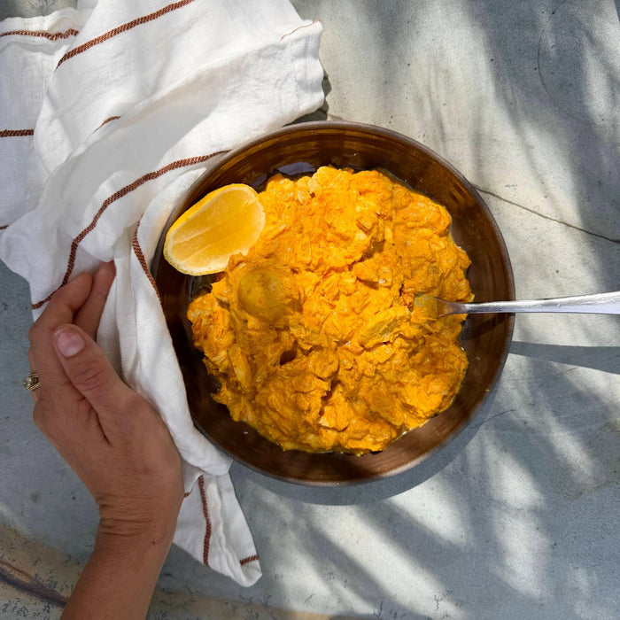 Bowl of white fish in yellow sauce with a lemon wedge on a textured surface